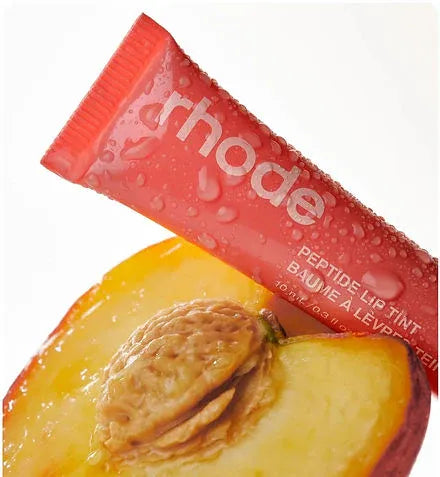 Tube of 'rhode' lip balm with a peach slice below on a white background